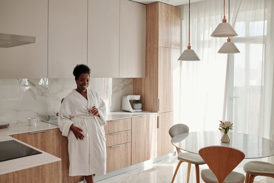 A cheerful woman in a bathrobe stands in a sunlit modern kitchen, embracing morning vibes.