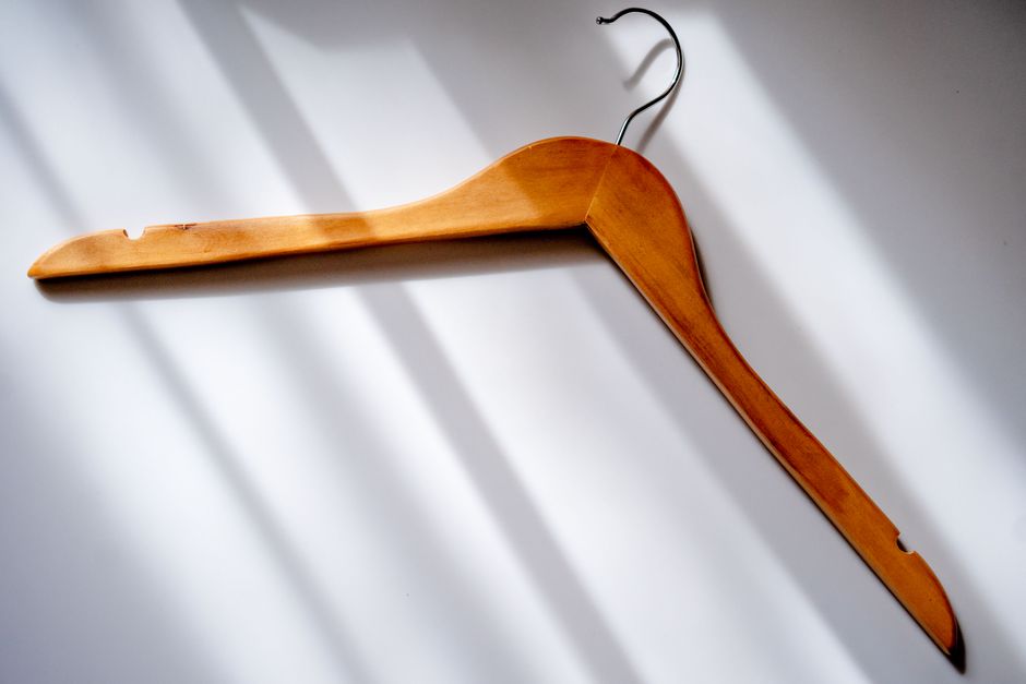 Minimalist image of a wooden clothes hanger casting shadows on a white surface.