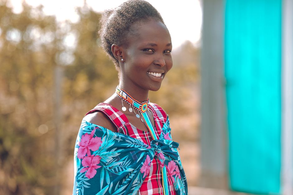 A woman in traditional attire smiles outdoors, showcasing vibrant patterns.