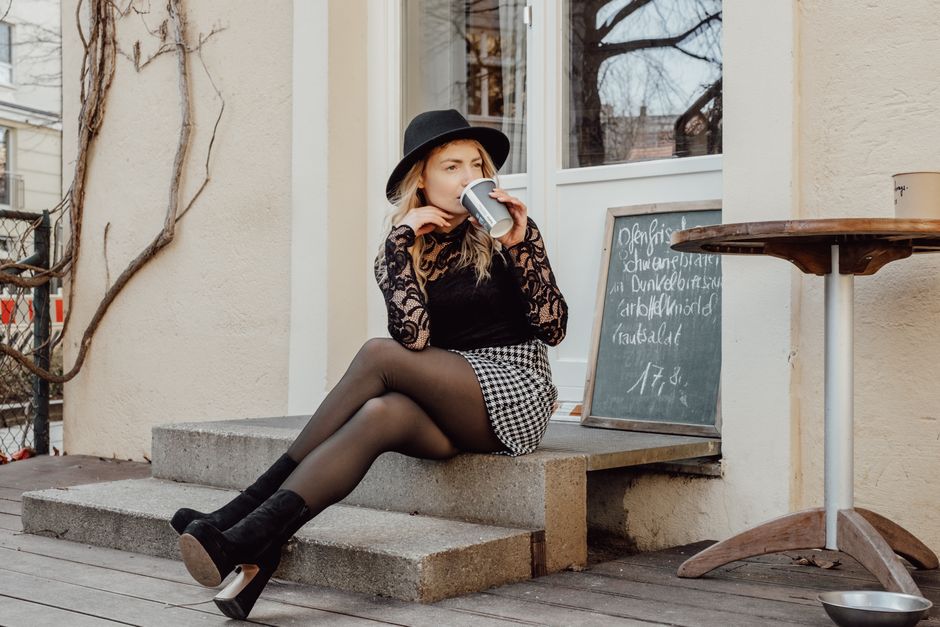 Fashionable woman in urban setting enjoying coffee on steps, showcasing modern style.