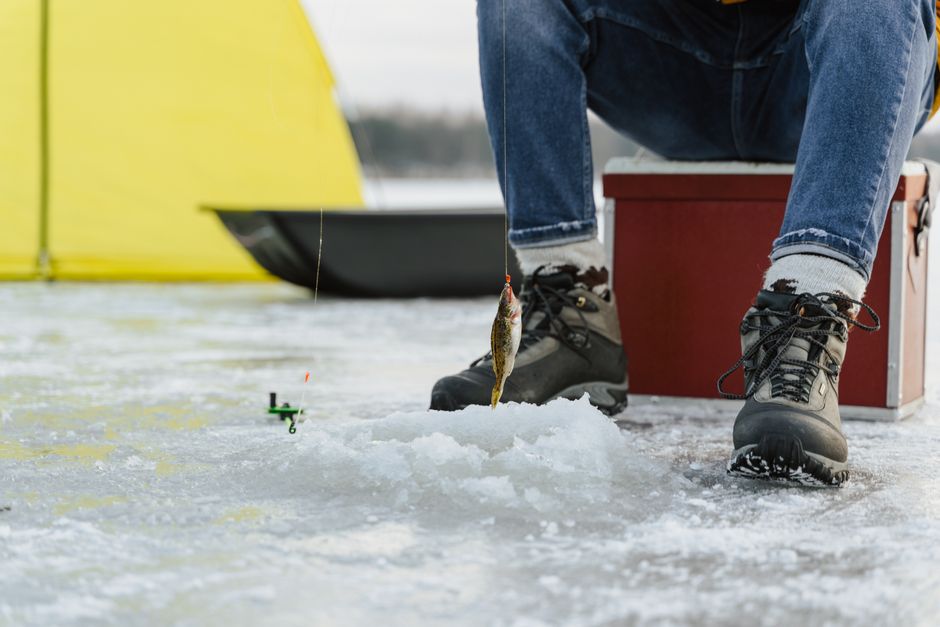 A man enjoys ice fishing on a frozen lake during winter with a catch on the line.
