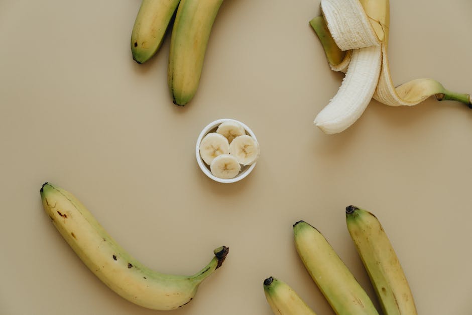 Top view of whole and sliced bananas artfully arranged on a neutral background.