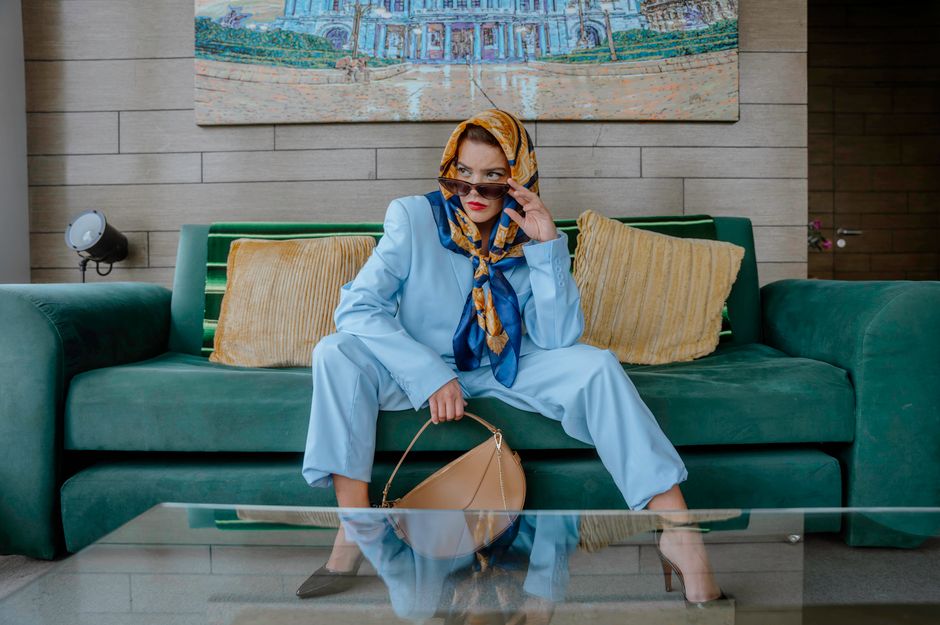 Fashionable woman in blue suit with scarf sitting on a couch in Ciudad de México. Chic and stylish.