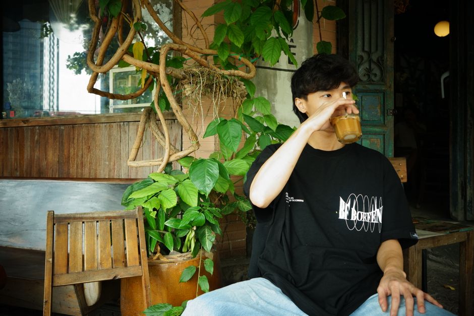 Relaxed young man sipping coffee in a cozy café with lush plants around.