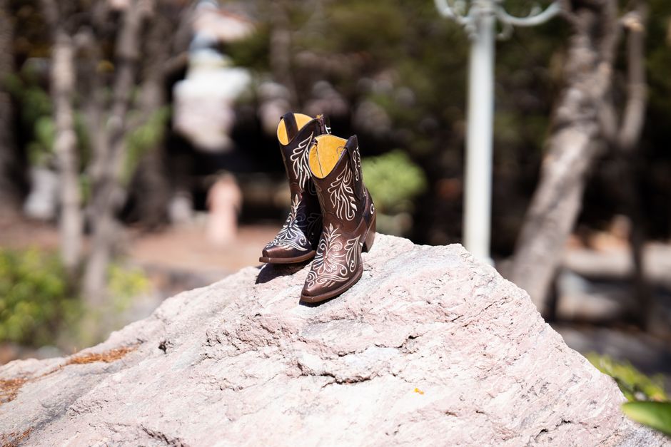 Pair of intricately designed cowboy boots sit on a rock, showcasing western fashion style.