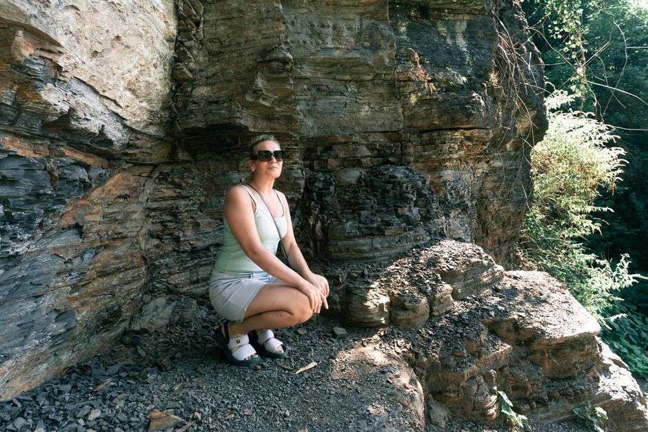 Woman crouching beside a rocky cliff in a sunlit outdoor environment, embodying adventure and exploration.