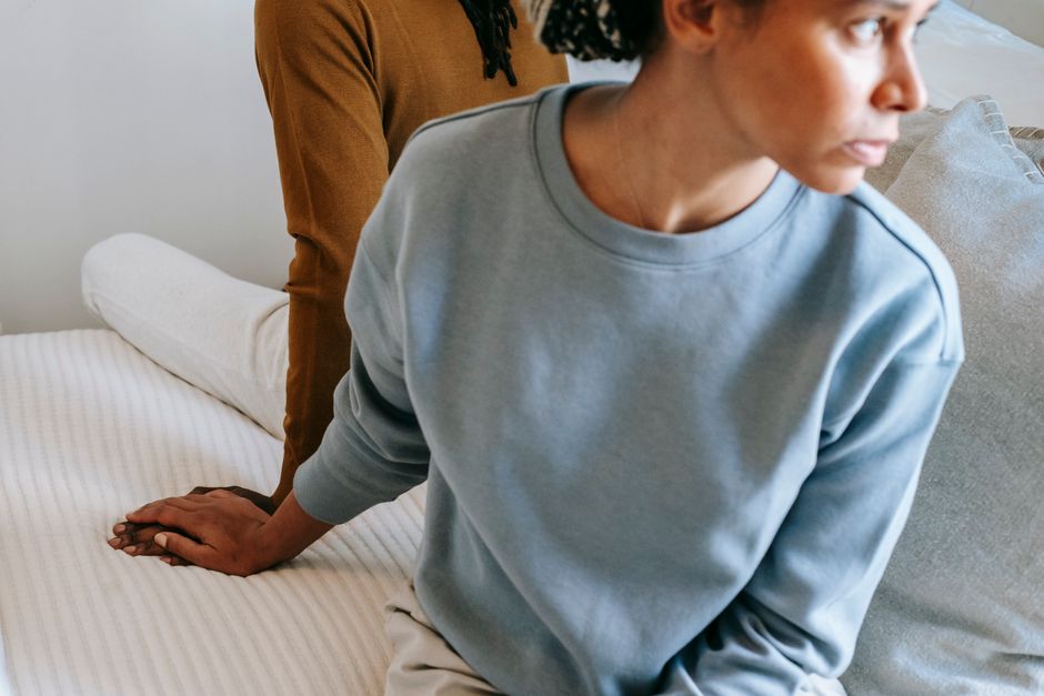High angle of young black couple wearing casual clothes sitting on bed with sad face while holding hands at home in daytime