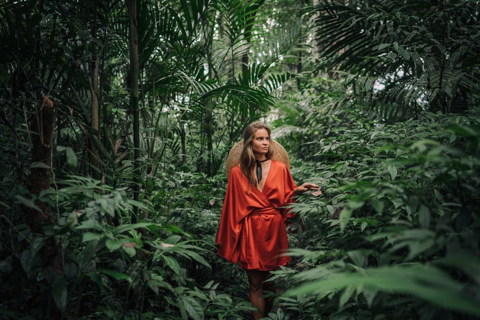 A woman in a red dress explores a dense tropical jungle, surrounded by lush greenery.