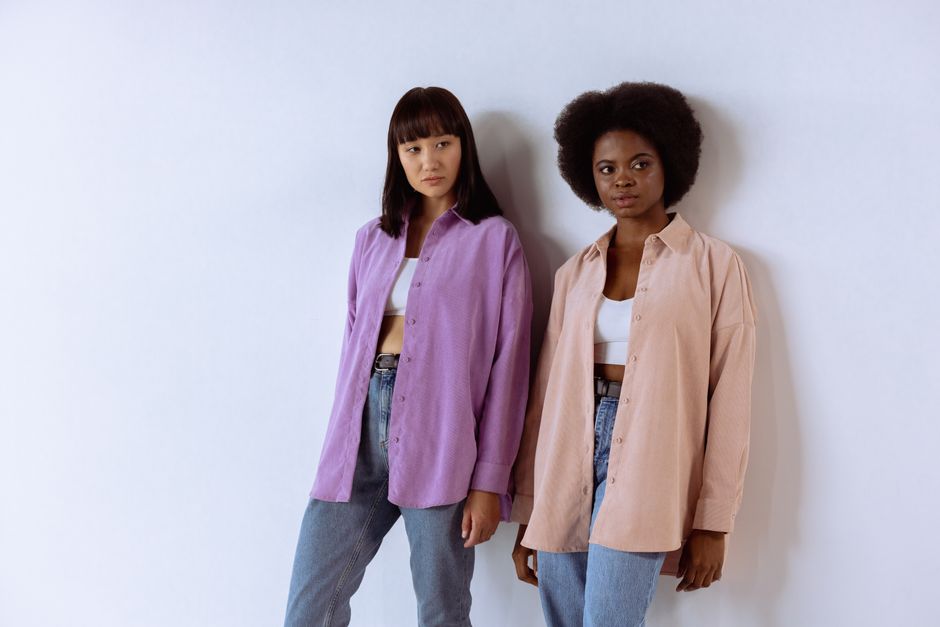 Two fashionable women posing in casual outfits against a white wall in an indoor studio.