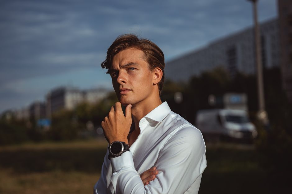 Portrait of a young man in white shirt outdoors, exuding a contemplative mood against an urban backdrop.
