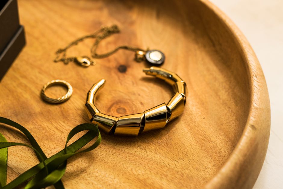 Close-up of stylish gold jewelry including a bracelet, ring, and pendant on a wooden tray.