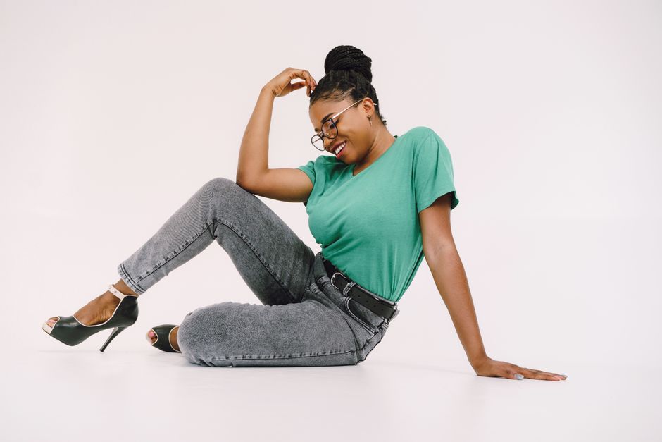 Smiling woman in a green top and jeans, sitting confidently in a studio on a white background.