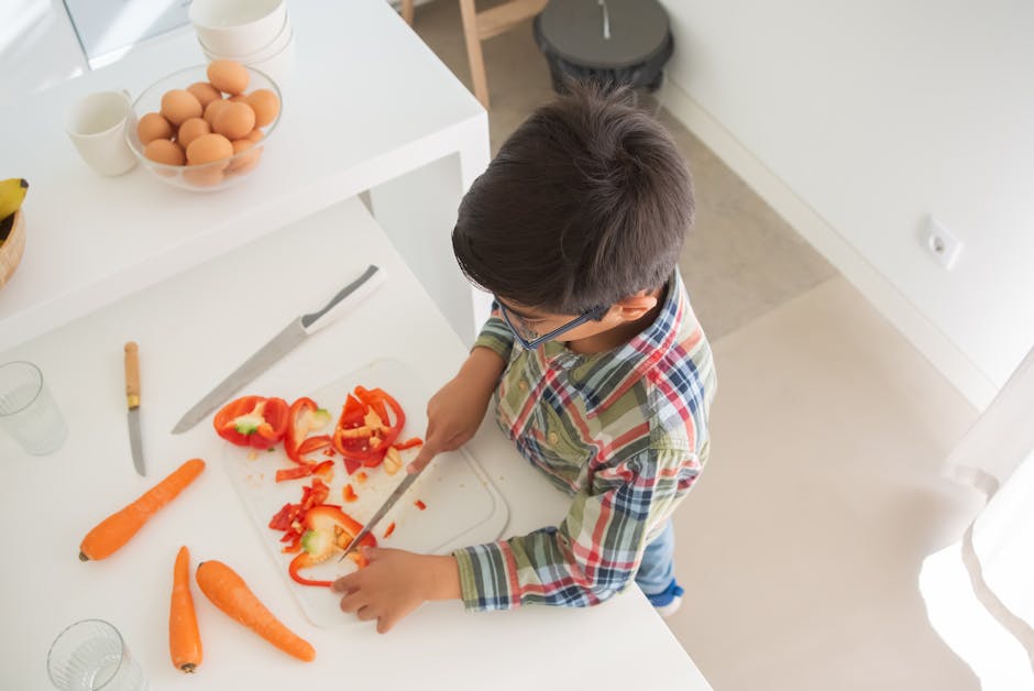 A child in a checkered shirt slices vegetables on a chopping board in a modern kitchen.