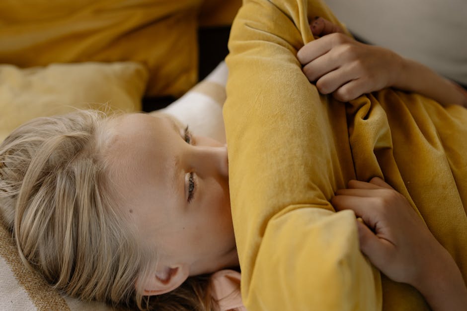 A child with blonde hair lying down, holding a yellow pillow, indoors.