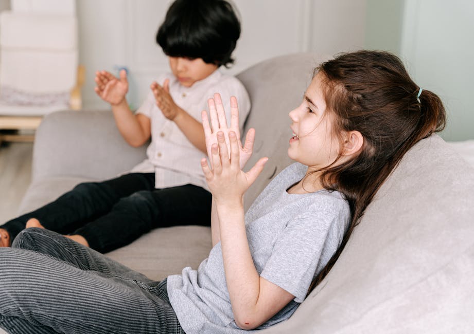Two children happily playing and clapping hands while sitting on a comfortable indoor sofa.