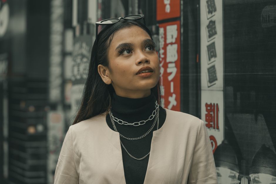 Stylish woman with sunglasses on head and silver chains, looking up against an urban background.