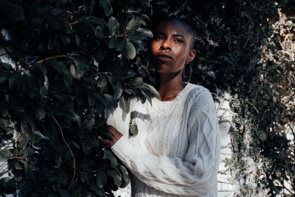 Captivating portrait of a stylish woman in a white sweater surrounded by lush greenery.