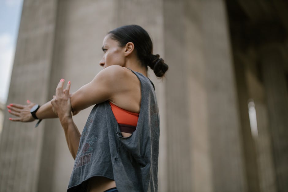 Woman in athletic wear stretching outdoors in a cityscape background.