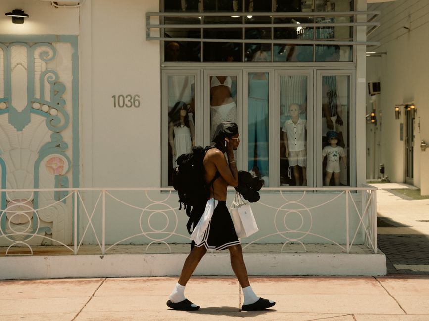 Man walking past a Miami boutique carrying shopping bags in the summer sun.