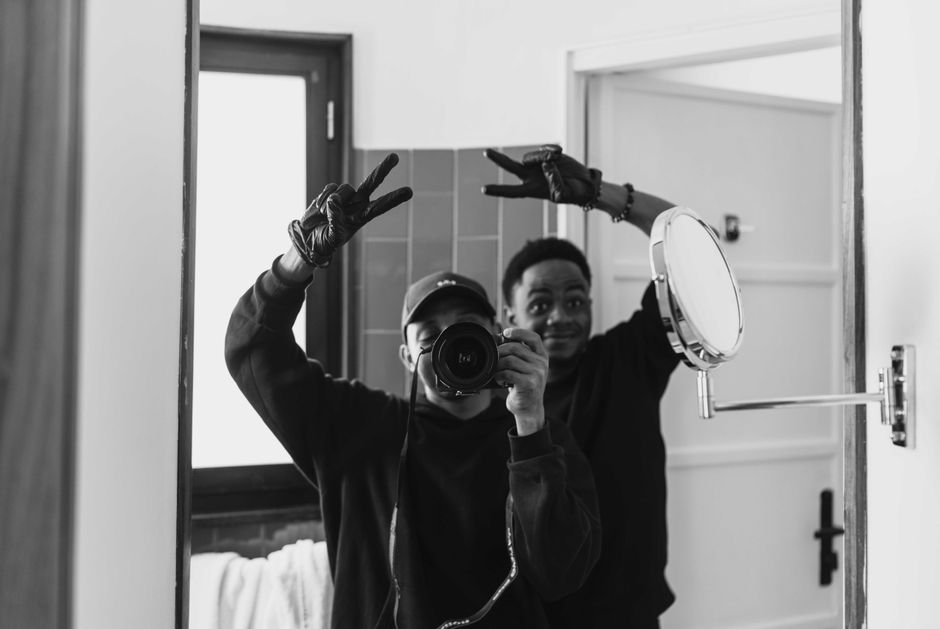 Two adults taking a playful selfie in a mirror, making peace signs in a bathroom.