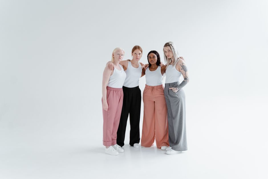 A group of diverse women wearing casual attire standing together in a studio embracing each other.
