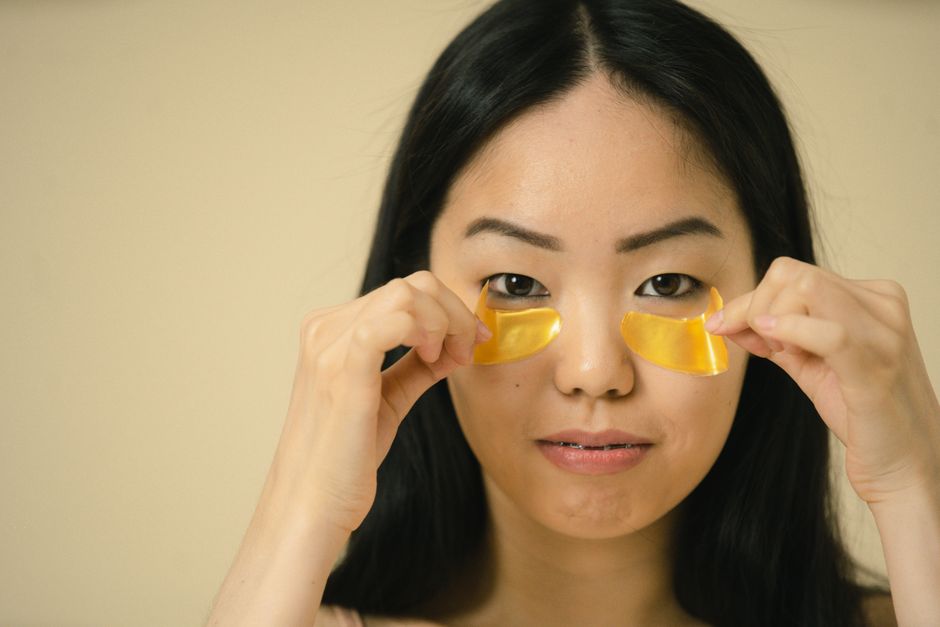Close-up of a woman applying golden eye patches during her skincare routine, highlighting beauty and self-care.