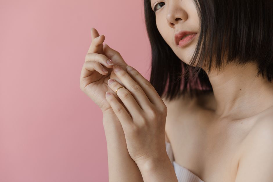 Close-up portrait of a woman gracefully posing with her hands against a pink background.