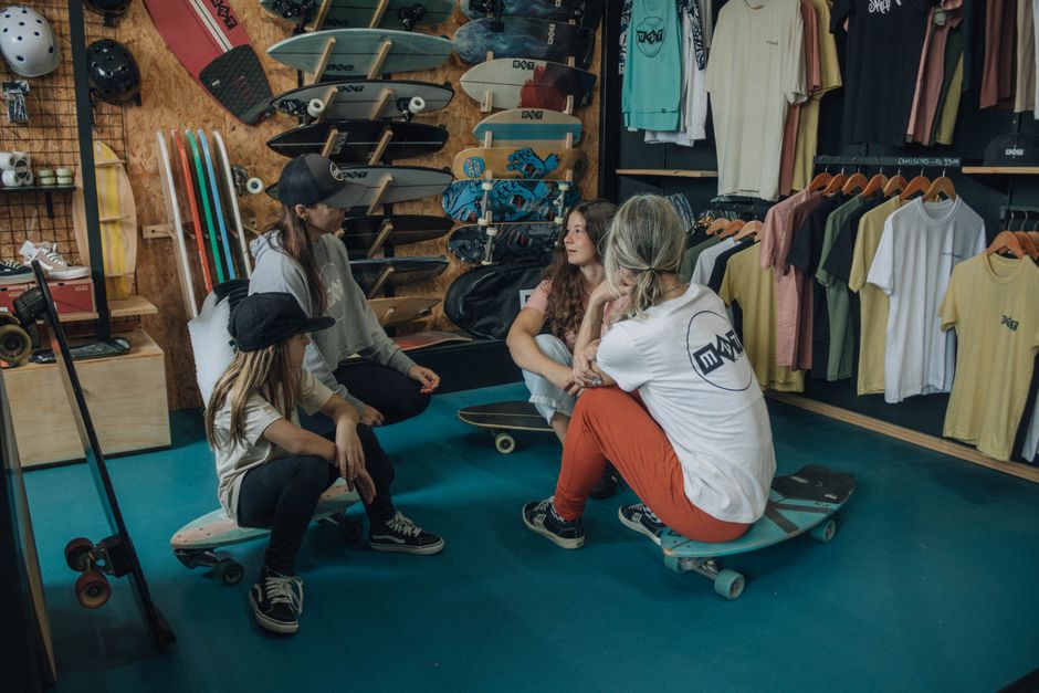 Group of adults conversing in a trendy skate shop surrounded by skateboards and apparel.