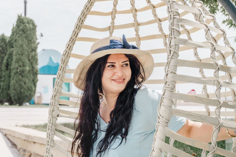 Charming woman in a hat relaxes in a swing chair on a sunny day in Baku, Azerbaijan.