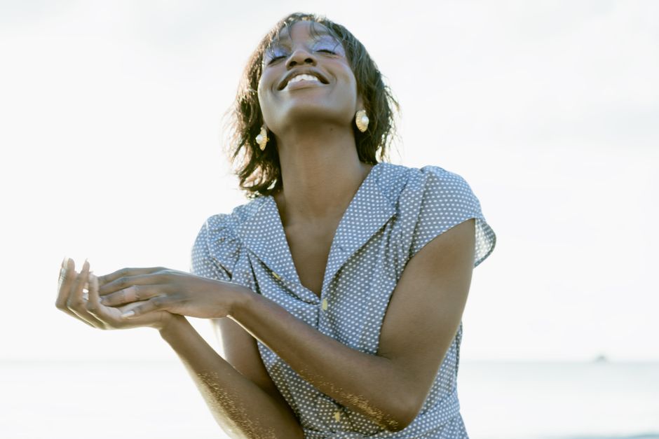 A smiling woman enjoys the outdoors, wearing a polka dot dress with her hands gracefully uplifted.