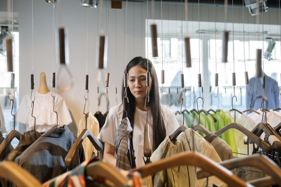Woman shopping in clothing store, exploring various outfits on hangers.