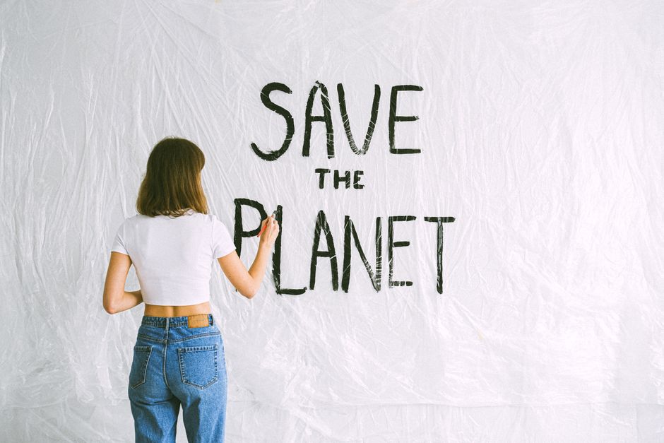 Back view of a woman with brown hair writing 'Save the Planet' on a white background with a plastic sheet.