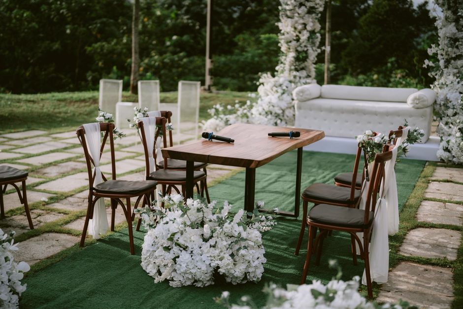 Charming outdoor wedding arrangement with chairs, table, and flowers on a green lawn.