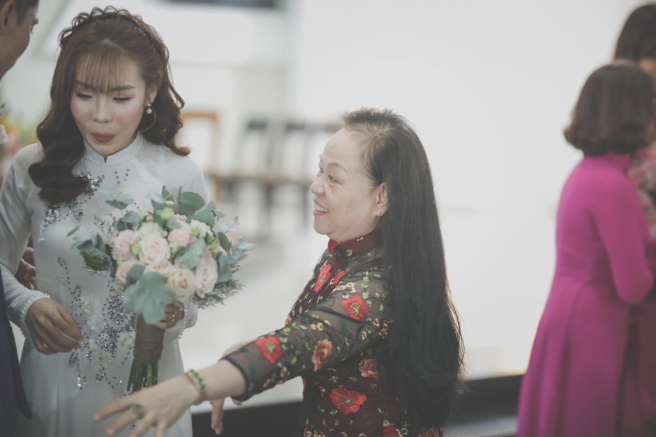 Bride in elegant wedding dress holding a bouquet, interacting with guests indoors.