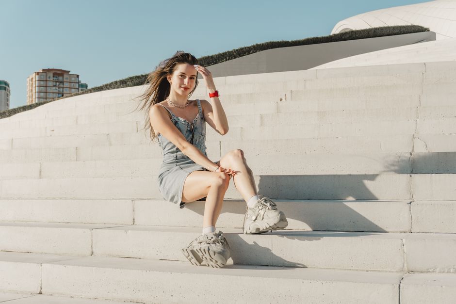 Young woman in casual attire sits stylishly on modern architectural steps with a sunny backdrop.