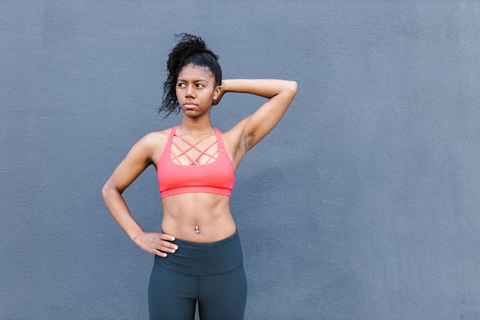 Confident athletic woman posing against a concrete wall in red sports bra and black leggings.