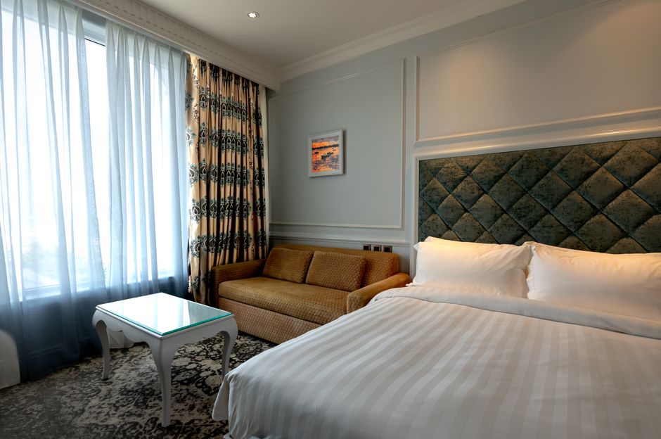 Luxurious hotel room featuring a plush bed, sofa, and patterned curtains creating a cozy ambiance.