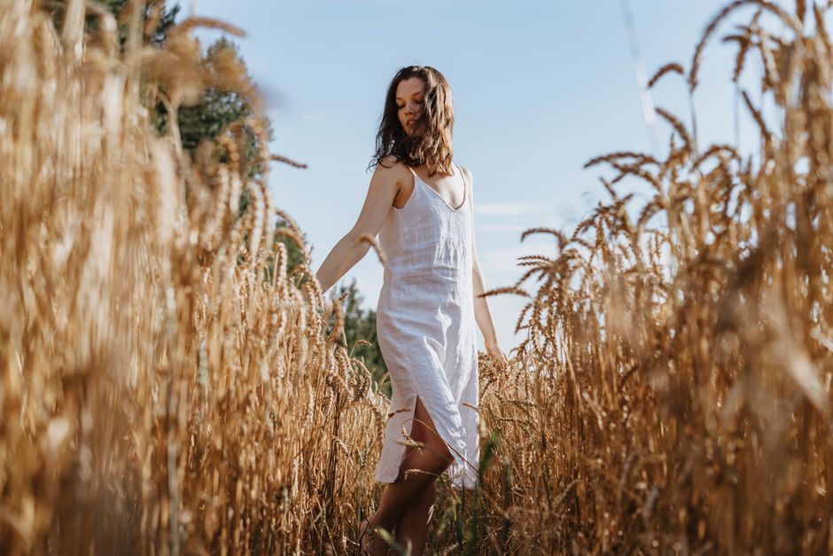 A woman in a white dress walks through a golden wheat field under a clear blue sky, evoking a sense of tranquility.
