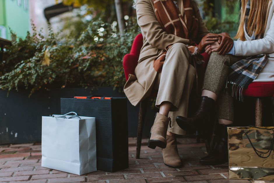 Cozy autumn day with two women sitting outdoors with shopping bags and fashionable boots.
