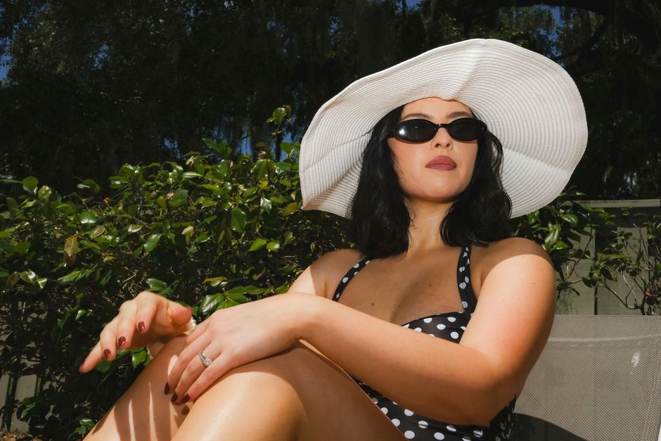 Stylish woman in a polka dot swimsuit and sun hat relaxing on a sunny day outdoors.