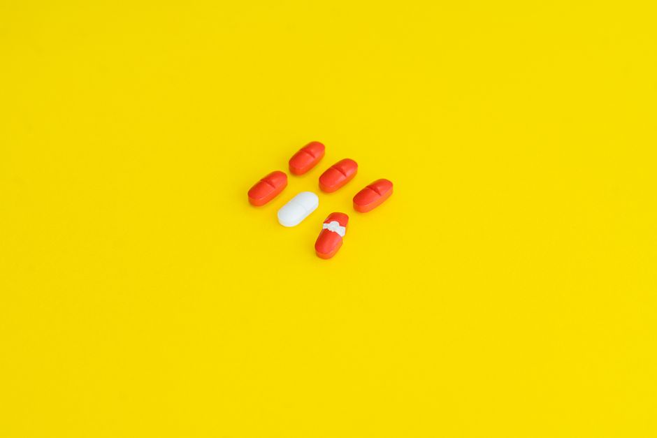 Close-up of red and white capsules arranged on a vivid yellow surface.