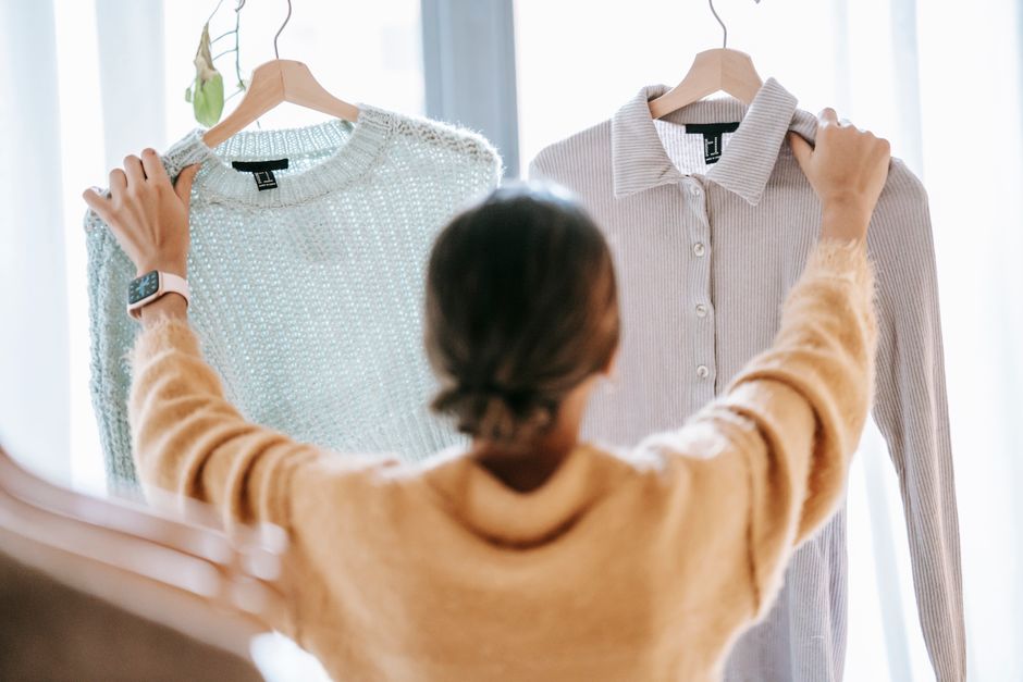 Back view of anonymous dark haired female showing hangers with apparel while standing against window
