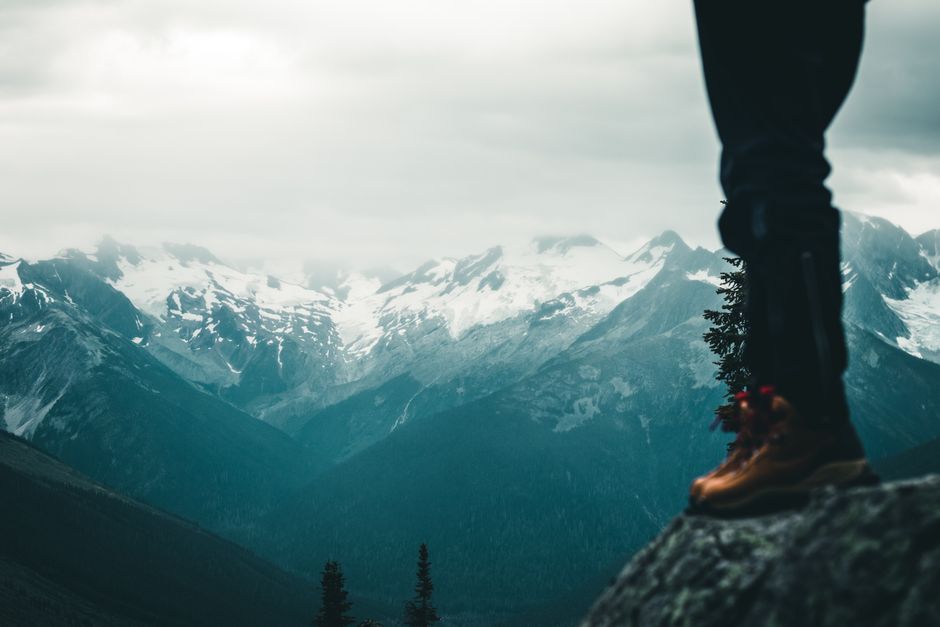 Person standing on a peak overlooking majestic snow-covered mountains in Canada.