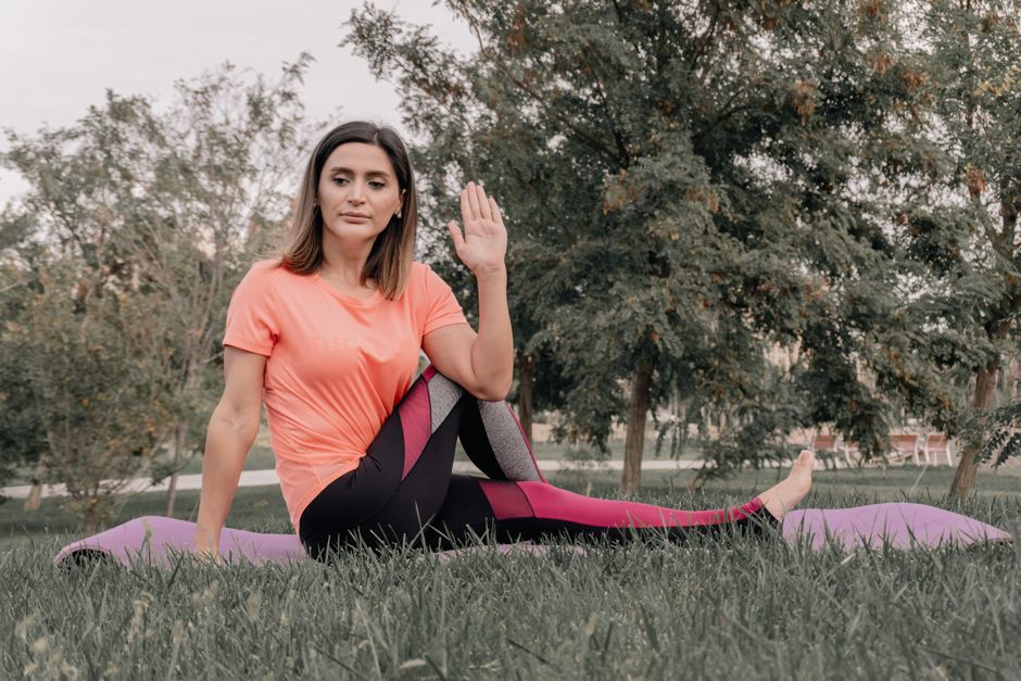 Adult woman practicing yoga on a mat in a park setting, displaying focused concentration.